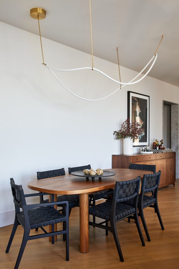 Pilled shaped wooden dining table with black chairs and accent lighting fixture.