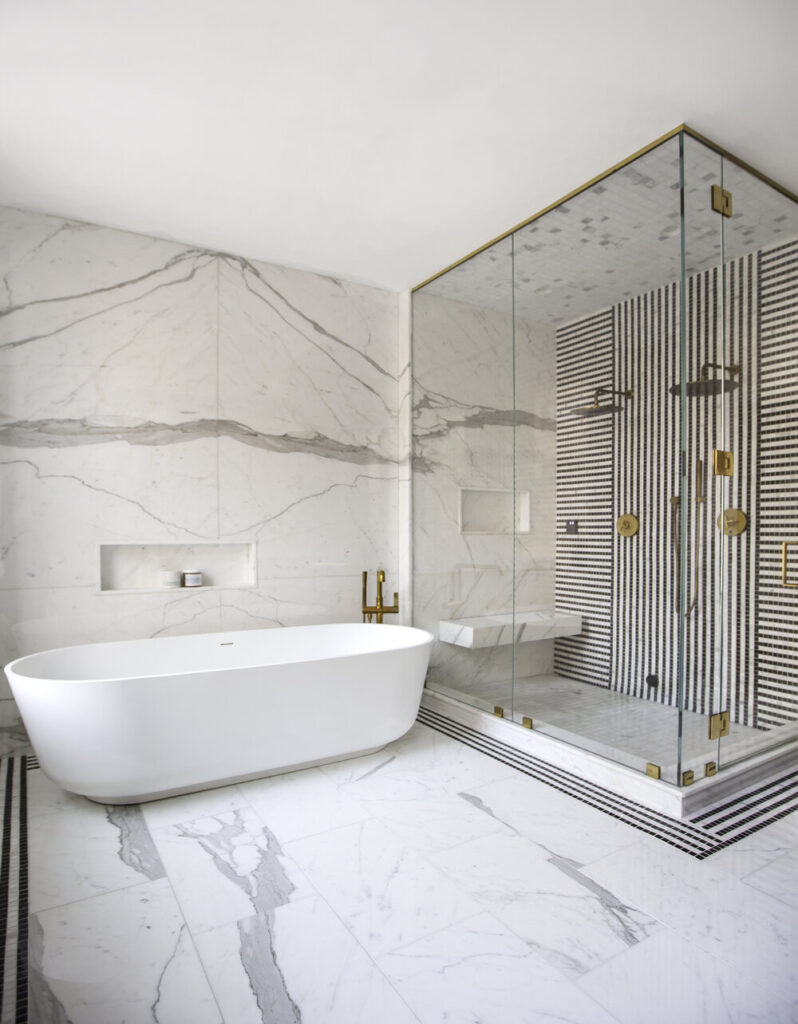 Luxury bathroom with white tub and shower, gold accents and marble flooring.