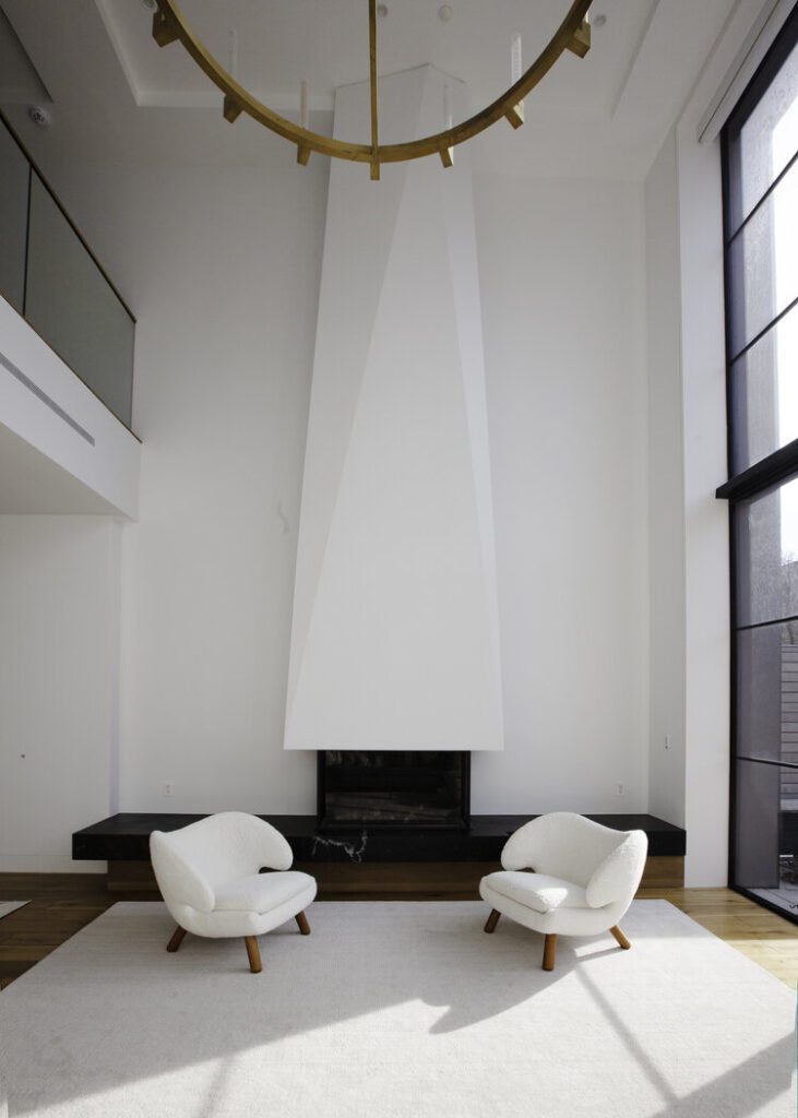 Two white chairs in a modern living room with a tall fireplace, designed for family-friendly living by Atelier Roux.